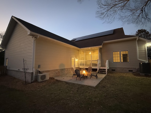 back house at dusk with a fire pit, central AC, a patio, solar panels, and ac unit