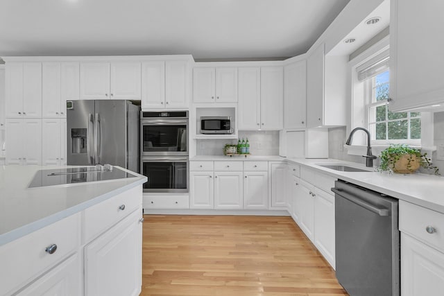 kitchen with sink, tasteful backsplash, stainless steel appliances, light hardwood / wood-style floors, and white cabinets