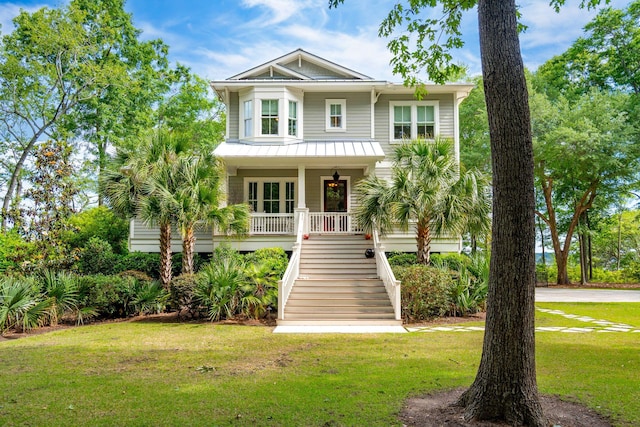 coastal inspired home featuring stairs, a porch, a front lawn, a standing seam roof, and metal roof