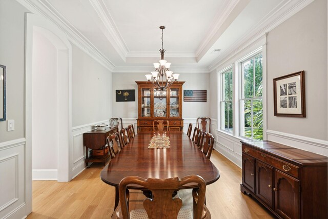 dining room with a chandelier, light wood-style floors, a raised ceiling, a wainscoted wall, and crown molding