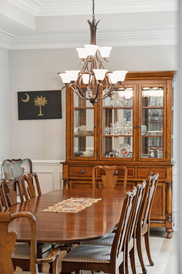 dining room with a chandelier, ornamental molding, a wainscoted wall, and a decorative wall
