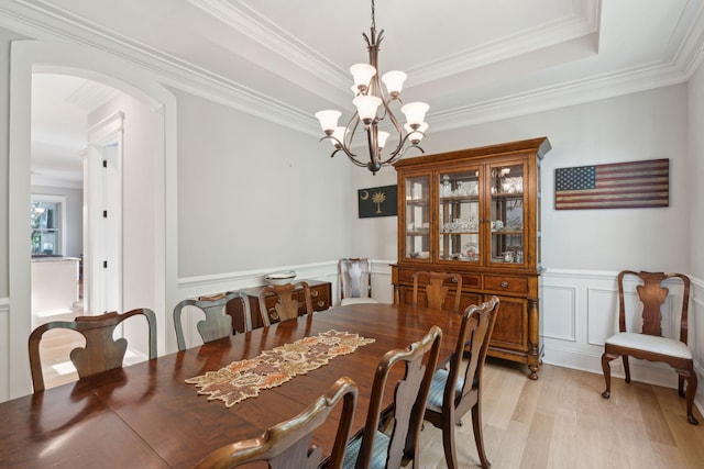 dining room featuring light wood-type flooring, ornamental molding, arched walkways, a decorative wall, and a chandelier