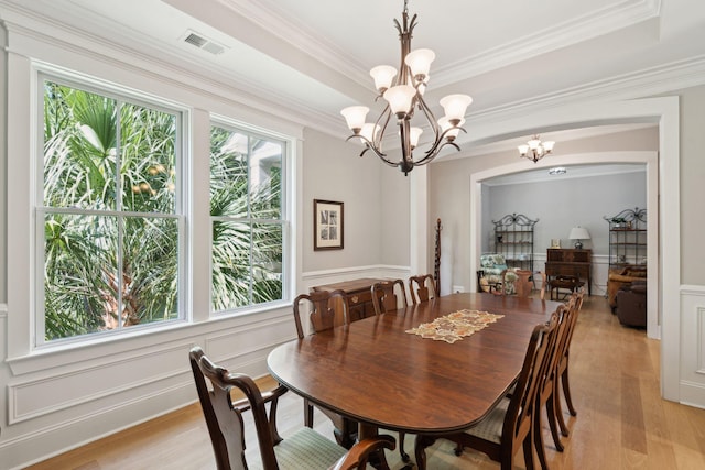 dining room with a chandelier, light wood-style floors, crown molding, a decorative wall, and wainscoting