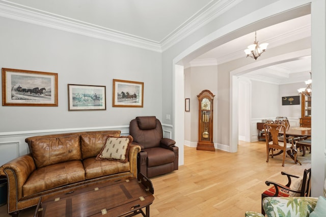 living room featuring a chandelier, arched walkways, crown molding, light wood-type flooring, and a wainscoted wall