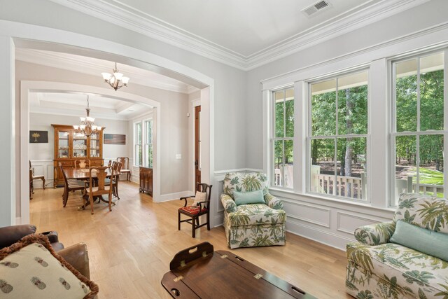 living area with a chandelier, light wood-style flooring, ornamental molding, arched walkways, and a wainscoted wall