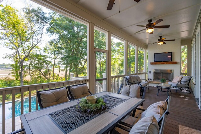 sunroom featuring ceiling fan, outdoor dining space, an outdoor living space with a fireplace, and lofted ceiling