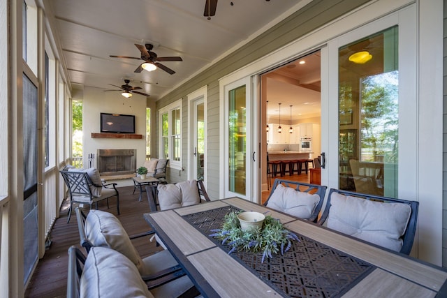 sunroom featuring ceiling fan, an outdoor living space with a fireplace, and outdoor dining space