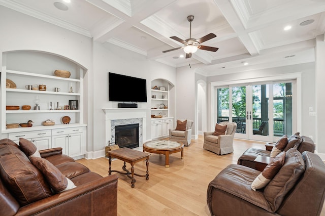 living room with light wood finished floors, beamed ceiling, a premium fireplace, a ceiling fan, and ornamental molding