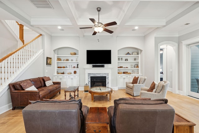 living room featuring ceiling fan, light wood finished floors, built in shelves, baseboards, and beamed ceiling