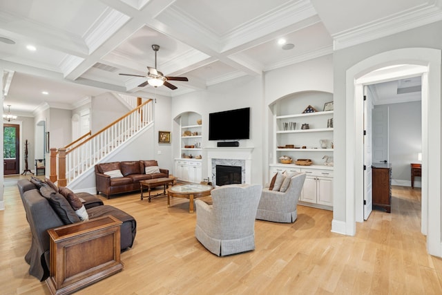 living area featuring ornamental molding, light wood finished floors, stairway, a fireplace, and beam ceiling