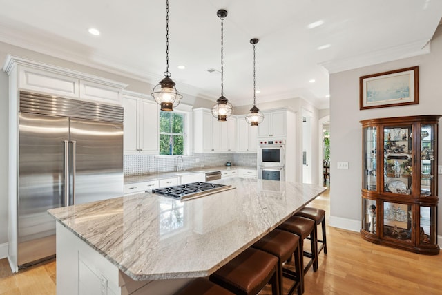 kitchen featuring stainless steel appliances, tasteful backsplash, white cabinetry, light stone countertops, and crown molding