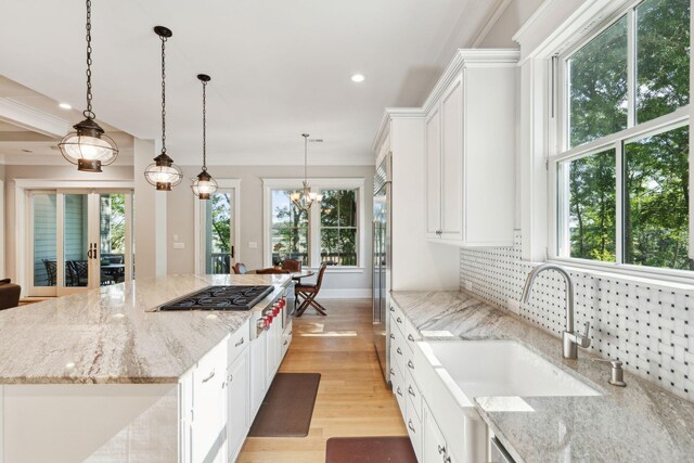kitchen featuring stainless steel gas cooktop, a sink, light wood-style flooring, white cabinetry, and healthy amount of natural light