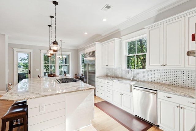 kitchen with appliances with stainless steel finishes, a sink, a center island, light wood finished floors, and white cabinetry