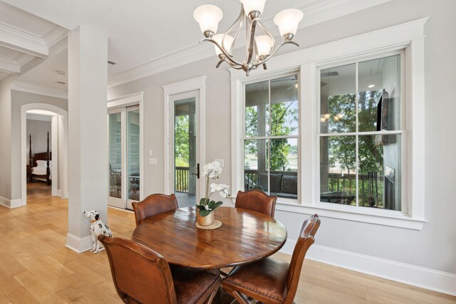 dining space with a chandelier, ornamental molding, arched walkways, light wood-type flooring, and baseboards