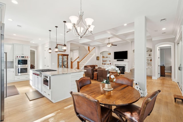 dining room featuring a glass covered fireplace, a chandelier, arched walkways, a ceiling fan, and built in shelves