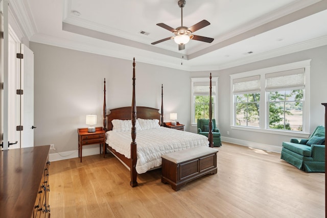 bedroom with light wood finished floors, a tray ceiling, baseboards, crown molding, and a ceiling fan