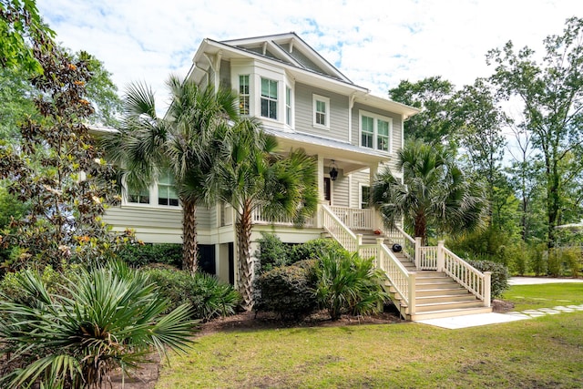 raised beach house featuring stairway, a front lawn, and covered porch