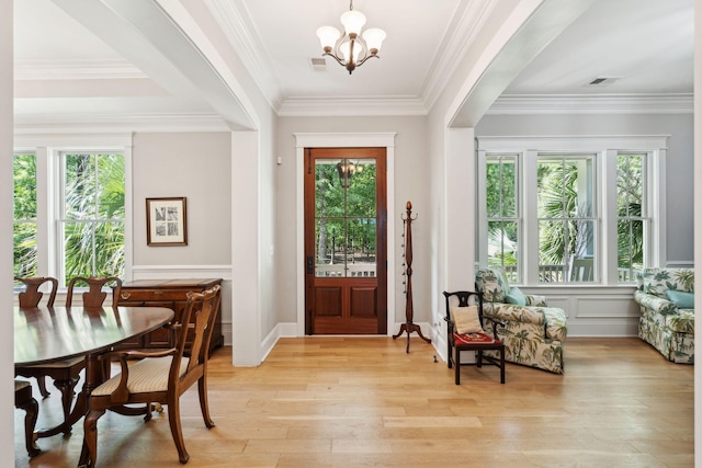 entrance foyer featuring light wood-style floors, a chandelier, ornamental molding, and a wainscoted wall