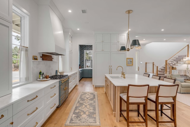 kitchen with an island with sink, custom range hood, white cabinets, and double oven range