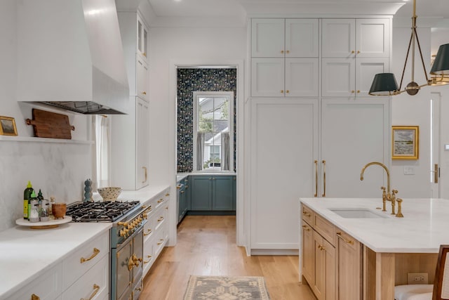 kitchen with wall chimney exhaust hood, sink, decorative light fixtures, light hardwood / wood-style flooring, and white cabinets