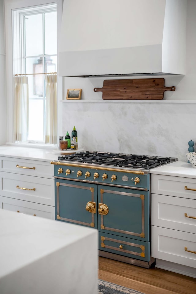 kitchen with range with two ovens, a healthy amount of sunlight, exhaust hood, and white cabinets