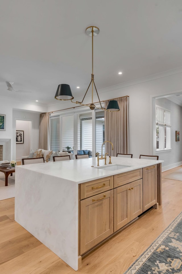 kitchen featuring decorative light fixtures, sink, a kitchen island with sink, light brown cabinets, and light wood-type flooring