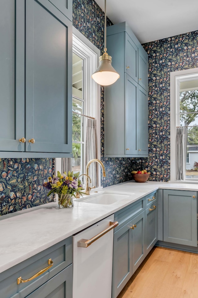 kitchen featuring stainless steel dishwasher, sink, hanging light fixtures, and light hardwood / wood-style flooring