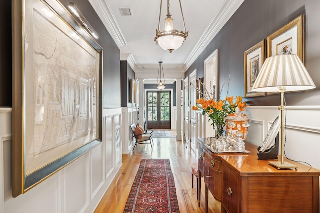 corridor with a wainscoted wall, light wood-style flooring, a decorative wall, and crown molding