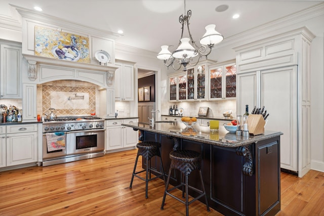 kitchen with glass insert cabinets, light wood-style floors, ornamental molding, and high end appliances