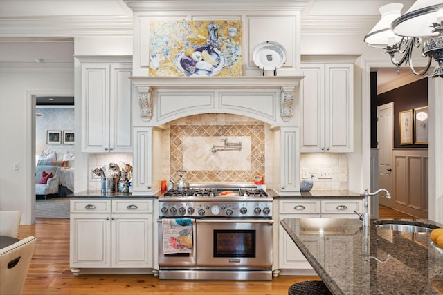 kitchen with light wood-style flooring, ornamental molding, a sink, dark stone counters, and double oven range