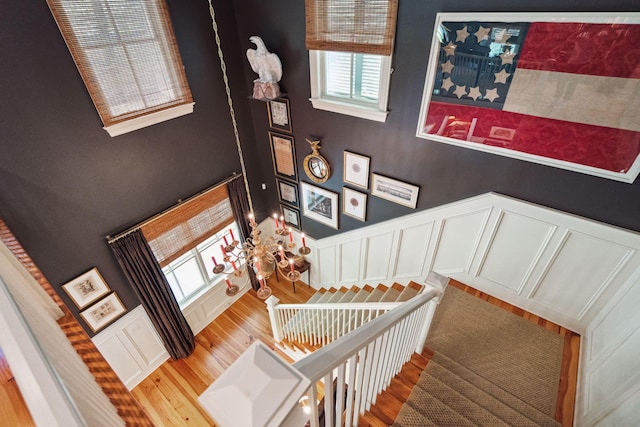 stairs with a decorative wall, wood finished floors, and wainscoting