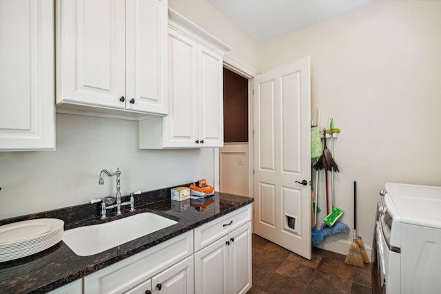 kitchen featuring white cabinets, a sink, dark stone counters, independent washer and dryer, and baseboards