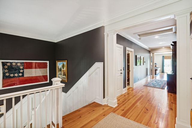 hallway featuring baseboards, ornamental molding, an upstairs landing, light wood-type flooring, and ornate columns