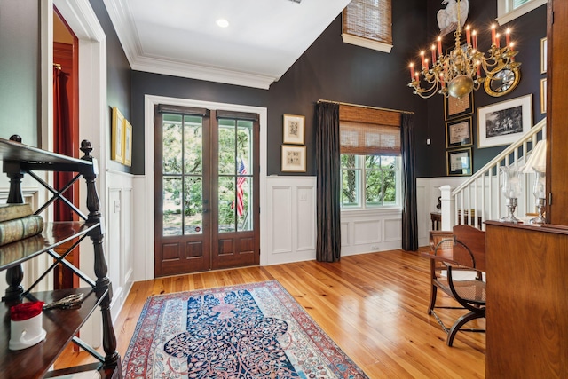 foyer entrance with french doors, a wainscoted wall, crown molding, stairway, and wood finished floors