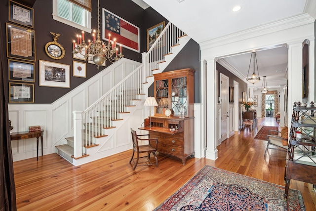 entrance foyer featuring wood finished floors, stairs, crown molding, ornate columns, and a decorative wall