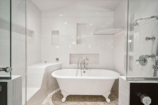 bathroom with a stall shower, vaulted ceiling, a freestanding tub, and tile walls