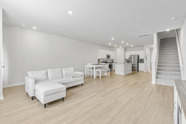 living room with light wood-type flooring, visible vents, stairway, and recessed lighting