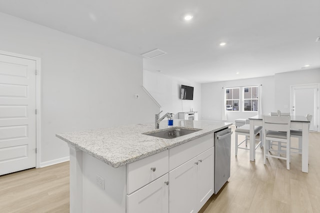 kitchen featuring a center island with sink, dishwasher, light stone countertops, white cabinetry, and a sink