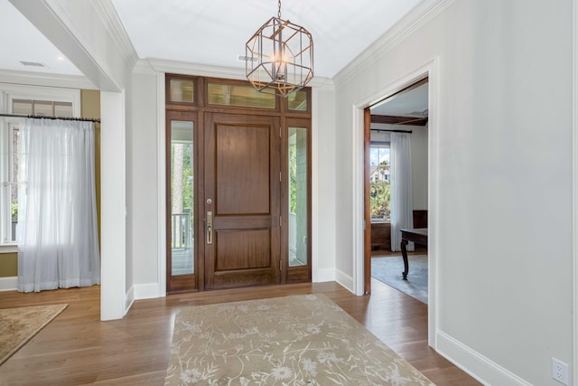 entrance foyer with plenty of natural light, wood finished floors, an inviting chandelier, and ornamental molding