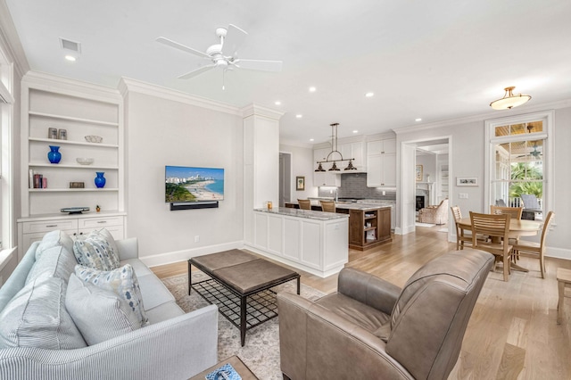 living room with visible vents, a ceiling fan, crown molding, and light wood-style floors