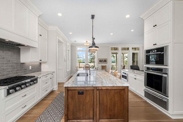 kitchen with a warming drawer, a sink, wood finished floors, stainless steel appliances, and white cabinets