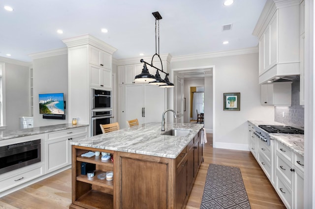 kitchen with light wood finished floors, an island with sink, white cabinets, stainless steel appliances, and a sink