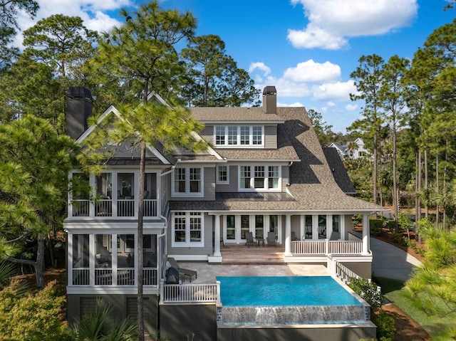 rear view of property featuring a patio area, a shingled roof, a chimney, and a sunroom