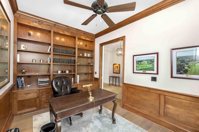 office area with built in shelves, ornamental molding, wainscoting, light wood-style flooring, and a ceiling fan