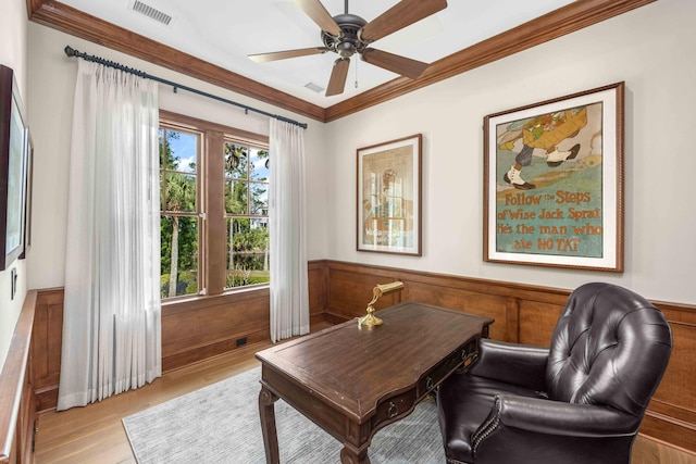 office space featuring visible vents, crown molding, a wainscoted wall, light wood-type flooring, and a ceiling fan