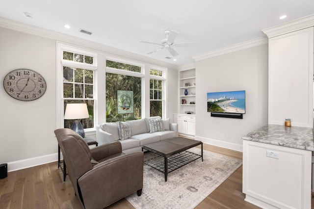 living area featuring visible vents, wood finished floors, baseboards, and ornamental molding