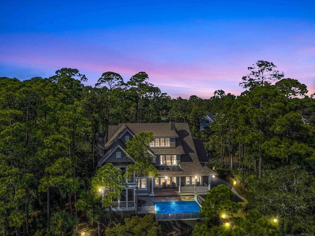 back of property featuring an outdoor pool, a view of trees, and a balcony