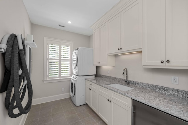 clothes washing area with visible vents, a sink, cabinet space, stacked washer / dryer, and baseboards