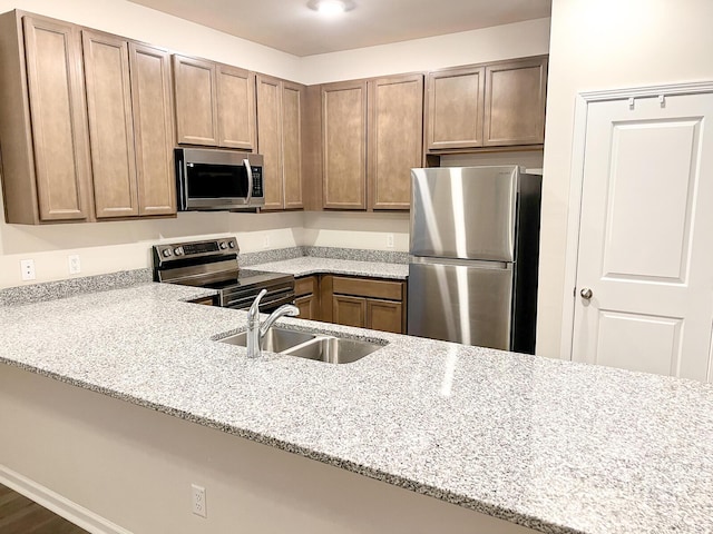 kitchen featuring sink, kitchen peninsula, light stone counters, and appliances with stainless steel finishes