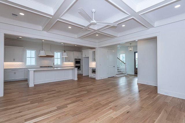 kitchen with white cabinets, light hardwood / wood-style floors, hanging light fixtures, and an island with sink